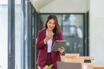 Smiling businesswoman in a suit communicating with a digital tablet using voice recognition and a stylus for modern technology