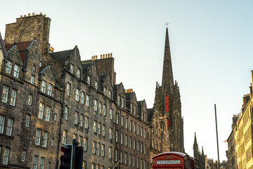 View of aged stone buildings stand shoulder-to-shoulder, culminating in a Tolbooth Kirk church spire in the Old Town with red phone cell, Edinburgh, Scotland, United Kingdom.