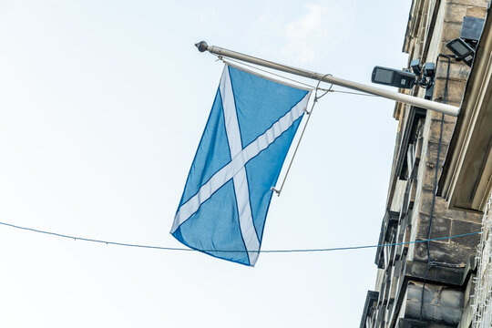 View of the Scottish flag fluttering gently against the pale sky, mounted on a weathered stone building, its colors a vibrant contrast, Edinburgh, Scotland, United Kingdom.