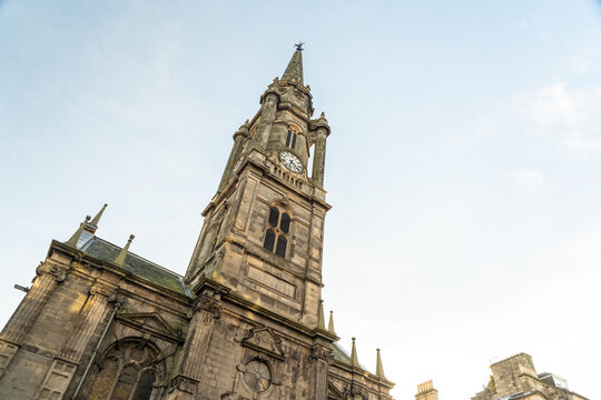 View of striking Tron Kirk stone church tower with a clock face rising towards the pale blue sky in the old town, Edinburgh, Scotland, United Kingdom.