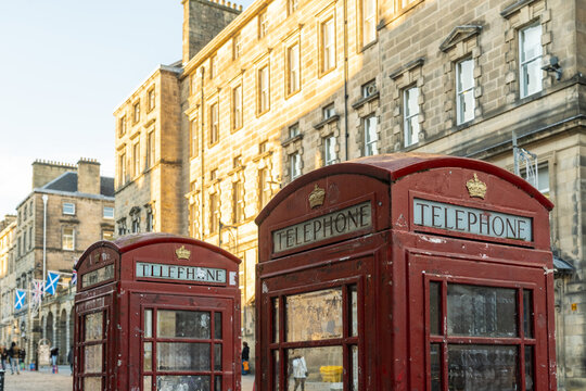 View of iconic red telephone boxes standing proudly against the backdrop of aged stone buildings bathed in warm sunlight, Old Town, Edinburgh, Scotland, United Kingdom.