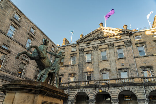 View of the bronze sculpture of Alexander and Bucephalus in front of the city hall building with flags fluttering against a clear sky, Edinburgh, Scotland, United Kingdom.