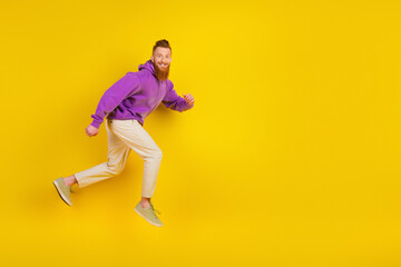 Happy young man in purple hoodie jumps against bright yellow background for stylish casual lifestyle fashion and advertising photo