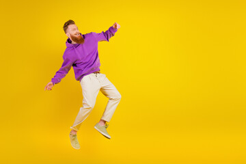 Fototapeta premium Young man in purple hoodie jumping with joy against bright yellow background