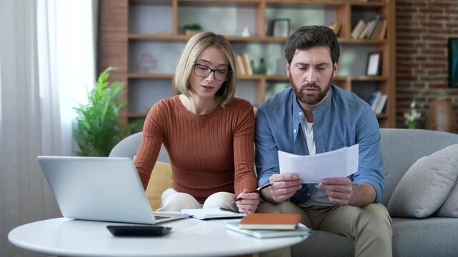 Thoughtful family couple is managing budget and home expense tracking while sitting at home office. Husband and wife is calculating money savings, paying bills online in application on laptop computer