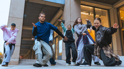 Group of street dancers practicing expressive moves in city plaza setting. Concept of casual clothing, youth marketing, lifestyle visuals, digital advertising campaigns.
