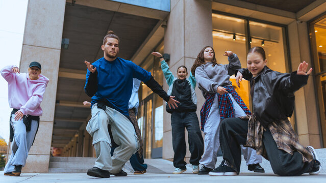 Group of street dancers practicing expressive moves in city plaza setting. Concept of casual clothing, youth marketing, lifestyle visuals, digital advertising campaigns.