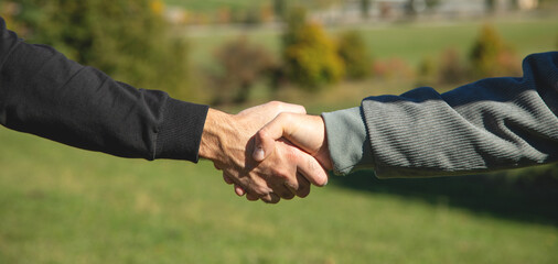 Two shaking hands in outdoors background.
