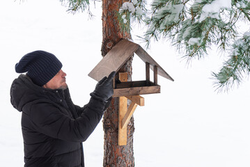 Man makes a bird feeder on pine tree in winter