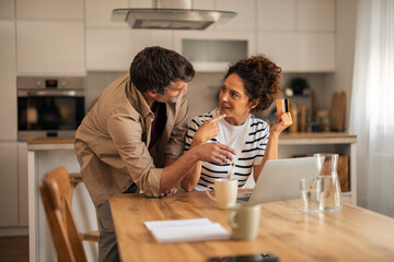 Casual Couple Discusses Finances at Kitchen Table With Laptop, Credit Card, and Coffee