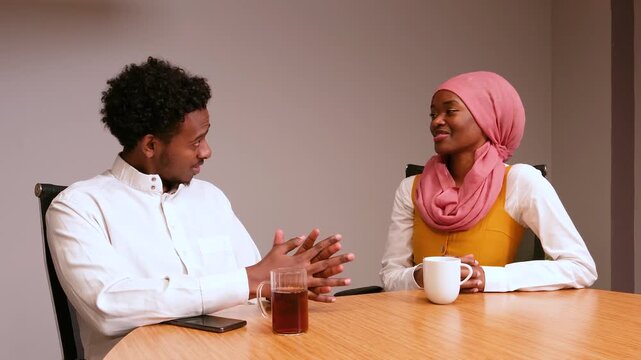 African Black Hijabi Woman and Black Man Wearing Glasses Having Friendly Conversation at Office Table with Tea and Coffee, Business Discussion, Diversity and Teamwork Concept