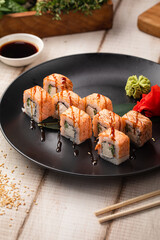 Philadelphia sushi rolls with creamy cheese, cucumber and seared salmon served on a black plate with wasabi