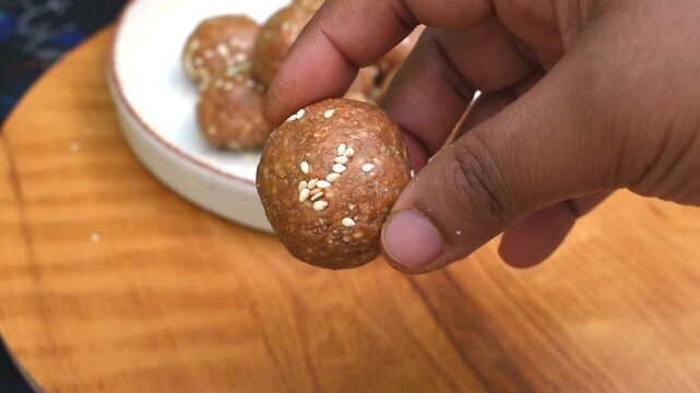 close-up of hand holding a til or sesame seed laddu. focus on hand and background blur. 