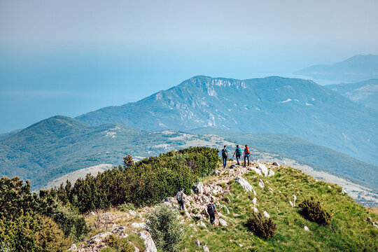 View of hikers silhouetted against the vast expanse of blue sea and sky, standing atop a grassy ridge, Mala Ucka, Primorje-Gorski Kotar County, Croatia.