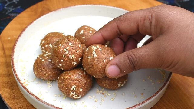 putting homemade til laddu in a plate served on a table for festive season. healthy sweet made with jaggery in place of sugar.