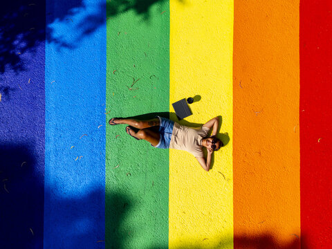 Aerial view of a person laying on rainbow pride design, bathed in sunlight, creating a vibrant spectrum against the urban canvas, Melbourne, Victoria, Australia.
