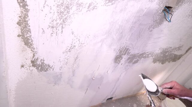 DIY home repair is demonstrated by a person applying spackle or joint compound to wall cracks and seams, smoothing the material for refinishing.