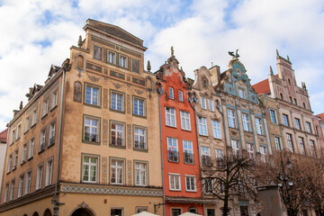 Old buildings with different colors sit next to each other on a busy street in a city known for its history. The sky is cloudy. A cobblestone street in Gdansk, Poland