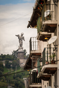 View of El Panecillo Virgin statue standing tall on a hill overlooking the city, contrasted with the quaint balconies of nearby buildings, Quito, Ecuador.