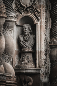 View of a weathered stone bust of a bearded man encased in an alcove, adorned with ornate carvings and spiraling columns, Quito, Ecuador.