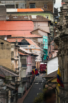 View of a steep city street adorned with colorful buildings and Ecuadorian flags fluttering gently, a ground-level perspective capturing the vibrant architecture, Quito, Ecuador.