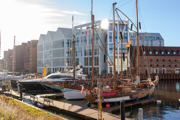 Historic ships are tied at a dock while modern buildings stand in the background under clear skies during the day. Gdansk, Poland