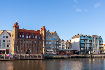 Obraz premium St. John's Gate (Brama Swietojanska). Colorful buildings line the waterfront in Gdansk Poland. The river under the blue sky.