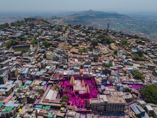 Aerial view of a vibrant gathering near the temple, where a sea of pink powder paints the joyful scene amid the architecture of Jyotiba Dongar, Maharashtra, India.