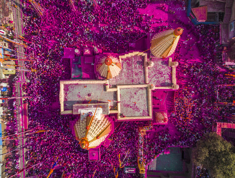 Aerial view of a temple complex awash in vibrant pink hues amidst a sea of devotees celebrating with colored powder, Jyotiba Dongar, Maharashtra, India.