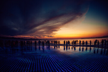 View of a mesmerizing scene unfolds as dusk descends, silhouetting figures against a backdrop of fiery skies and the illuminated ground, Zadar, Zadar County, Croatia.