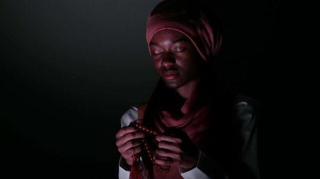 Cinematic low-key lighting portrait of a thoughtful young woman in a headscarf against a dark background, conveying deep emotion, introspection, modern identity, and dramatic atmosphere