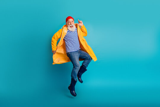 Elderly man jumping in yellow raincoat with striped shirt beanie blue background joyful retro style