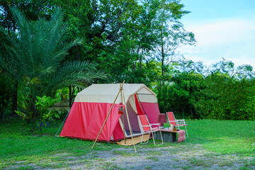 camping setup in the evening, vintage cabin tents, antique oil lamps, retro chairs, and a group of camping tents with outdoor coffee-making facilities on tables in a forest camping area.