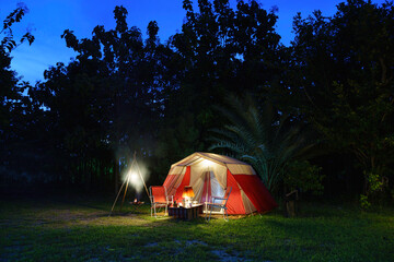 Camping tents at night, vintage cabin tents, antique oil lamps, retro chairs, and a group of camping tents with outdoor coffee-making facilities on wooden tables in a forest camping area.