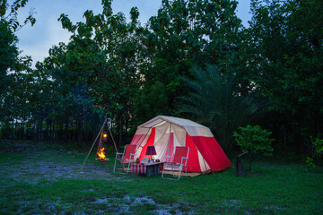 Camping tents at night, vintage cabin tents, antique oil lamps, retro chairs, and a group of camping tents with outdoor coffee-making facilities on wooden tables in a forest camping area.