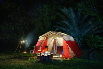 Camping tents at night, vintage cabin tents, antique oil lamps, retro chairs, and a group of camping tents with outdoor coffee-making facilities on wooden tables in a forest camping area.