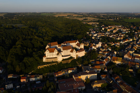 Aerial view of the imposing Colditz Castle, its white walls contrasting against the lush green forest and the town's terracotta roofs, Colditz, Sachsen, Germany.