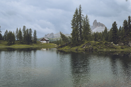 View of a serene lake mirroring the surrounding lush green forest and distant, jagged peaks under a cloudy sky, Croda da Lago, Veneto, Italy.