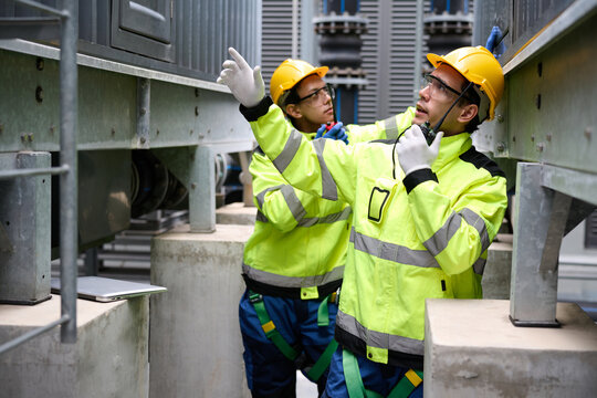 Engineers talk on a walkie talkie and inspecting machinery, wearing hard hats and safety gear in the factory