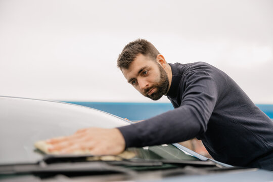 Focused man cleaning car windshield at car wash