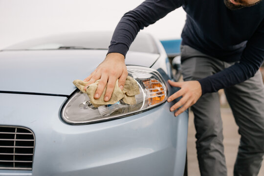 Detailed close-up of male worker wiping car headlight by hand as part of professional car wash and vehicle care process.