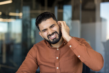 Young man experiencing severe ear pain, touching his ear with a visible grimace of discomfort,...