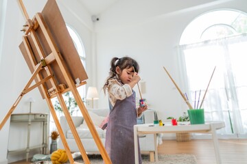 Child paints at home in bright room with easel and art supplies during afternoon activity