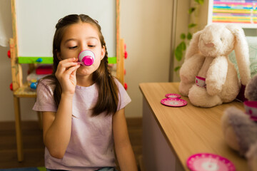 Little girl playing pretend serving tea to stuffed animal bunny during imaginative childhood game at home
