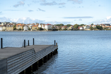 View of calm waters reflecting the sky with a wooden pier extending into the water near a line of colorful buildings, Karlskrona, Blekinge County, Sweden.