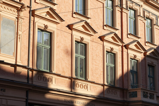 View of a sun-drenched, ornate building facade with peach-colored walls, triangular pediments, and green-framed windows casting strong shadows, Karlskrona, Blekinge County, Sweden.