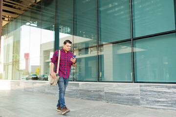Man strolling outdoors in the city, holding and looking at his smartphone, connecting with digital...
