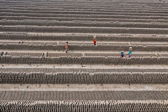 Aerial view of workers carefully arranging bricks in long, parallel rows, creating a textured landscape of uniform patterns, Dhaka, Dhaka Division, Bangladesh.