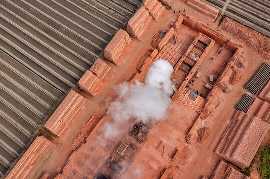 Aerial view of a brick factory with smoke billowing from the kiln, creating a stark contrast against the neatly stacked bricks, Dhaka, Dhaka Division, Bangladesh.