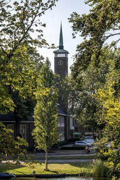View of a striking church tower rises beyond the lush green foliage and tranquil water in a ground photo, Alkmaar, North Holland, Netherlands.